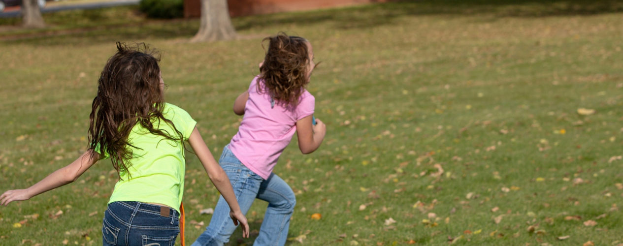 Two girls playing tag. One girl is running away and the other girl is chasing her.