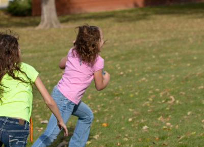 Two girls playing tag. One girl is running away and the other girl is chasing her.