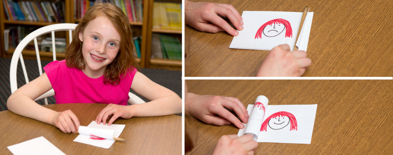 Little girl smiling at the camera as she colors. Two close up shots of what she's coloring include a smiling face and frowning face.