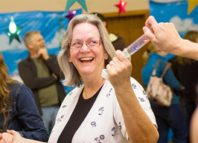 An older woman smiles joyfully as a baton she's holding lights up.