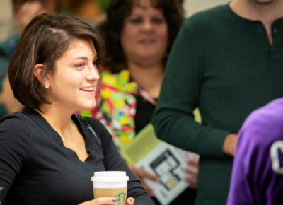 A woman is checking in for a conference with coffee in her hands.