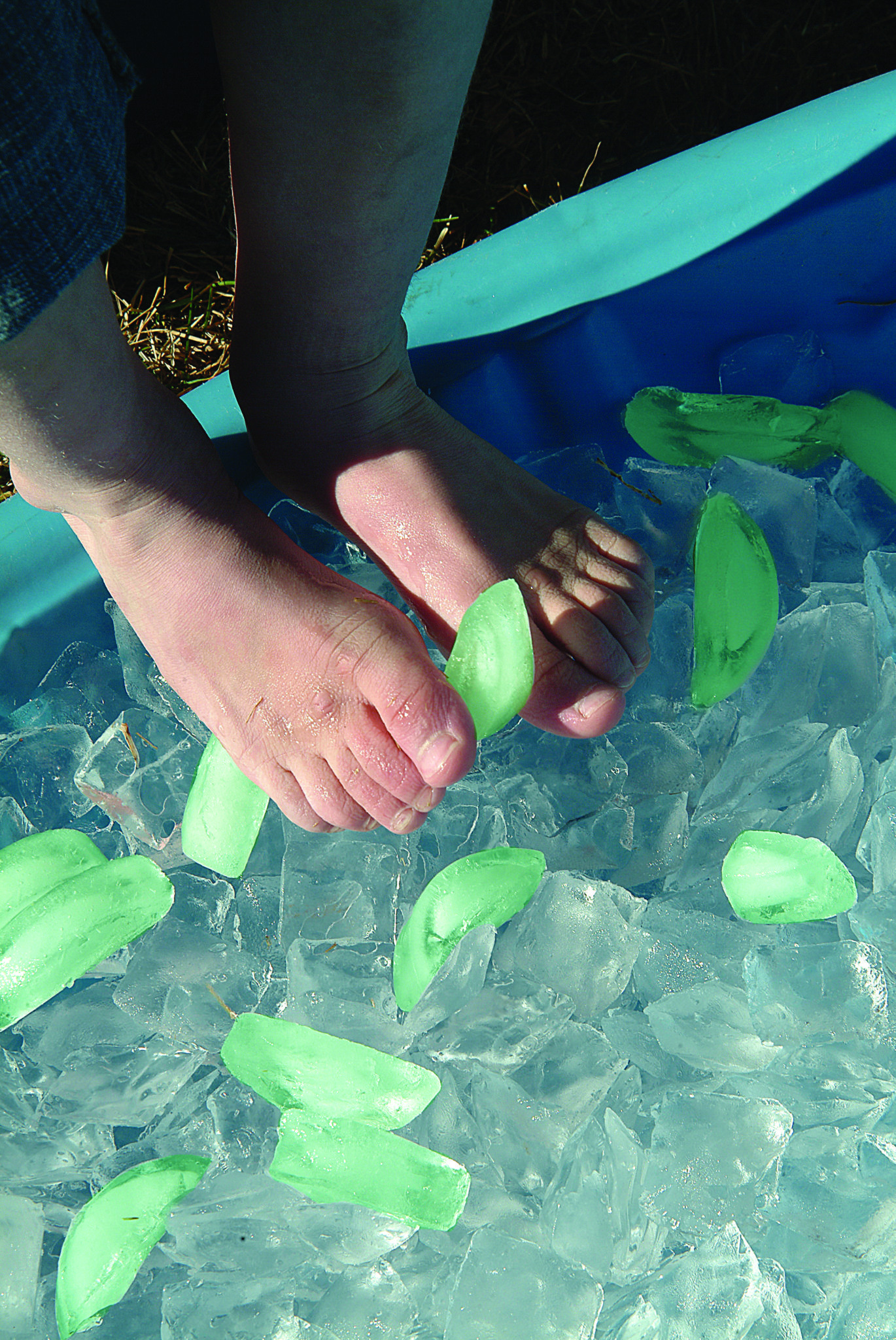 A child grabs colored ice cubes with their toes.