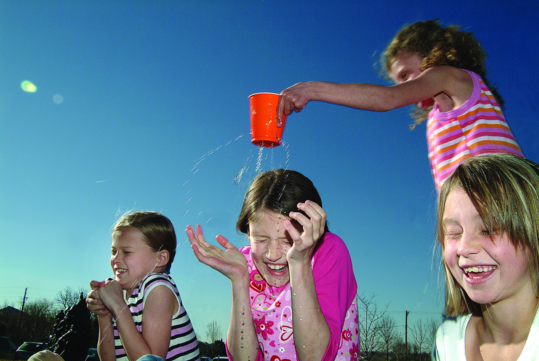 A child with a leaky cup walks around sprinkling friends with water.