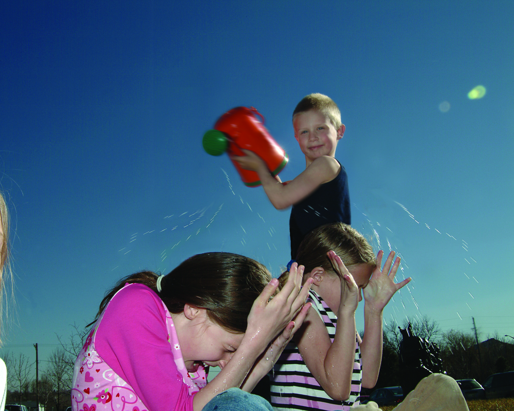 A boy sprinkles water out of a watering can on his friends.