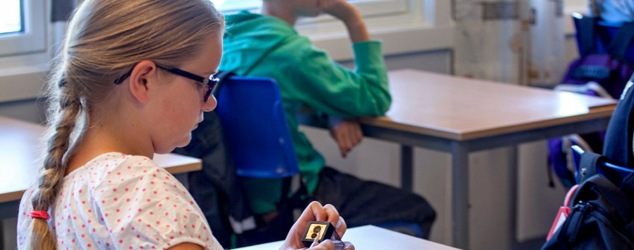 Preteen girl with braid and glasses sits at her desk sharpening a pencil.
