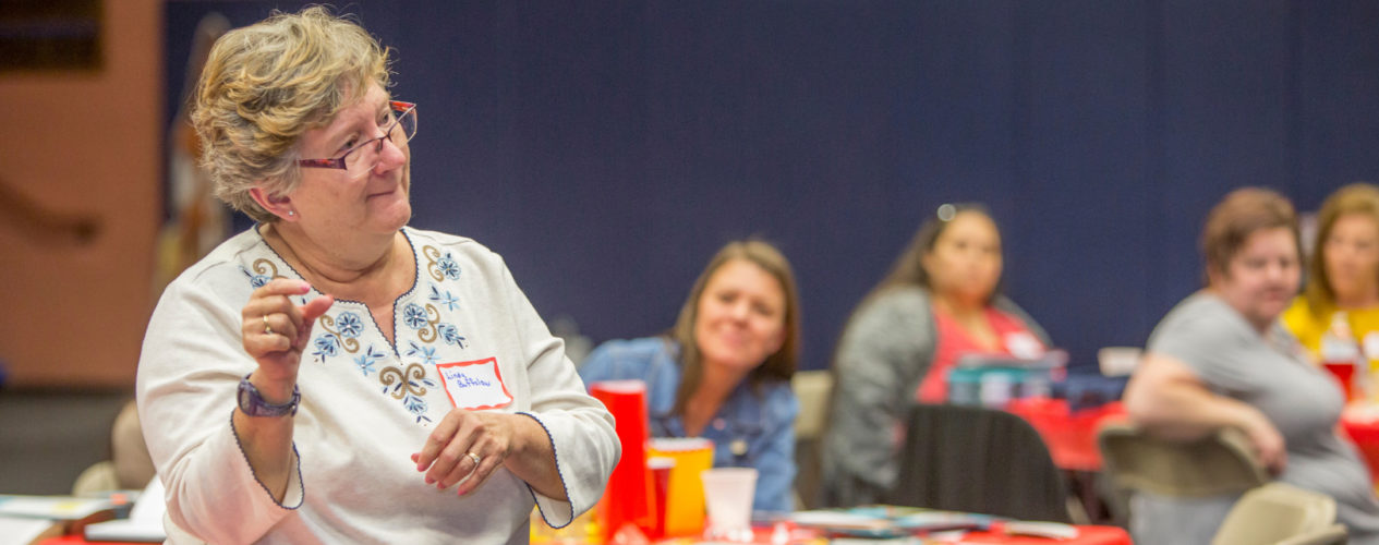 A older woman volunteer stands up and talks during a teacher training meeting.