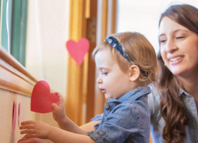 A mom is helping her toddler decorate with hearts.