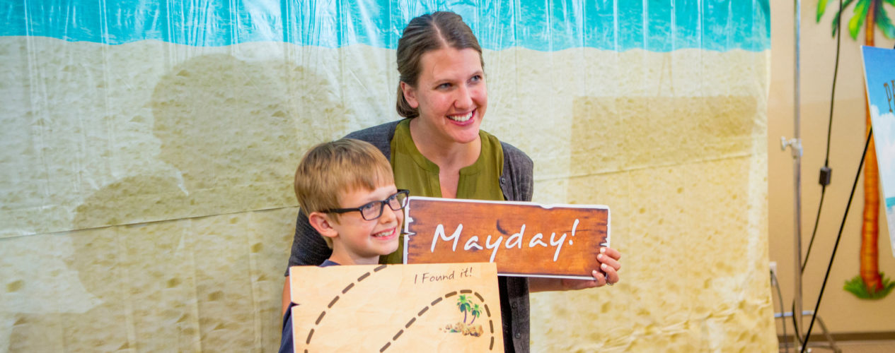 A kid and his mom take a picture together in a pirate-themed photo booth.
