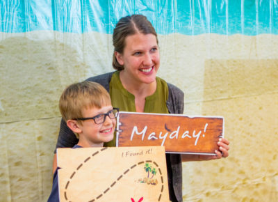A kid and his mom take a picture together in a pirate-themed photo booth.