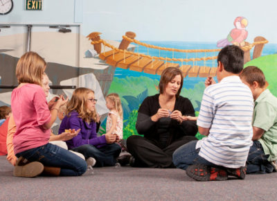 A small group of children gather around an adult leader in their church's children's ministry.