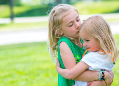 An elementary aged girl hugs a preschool girl.