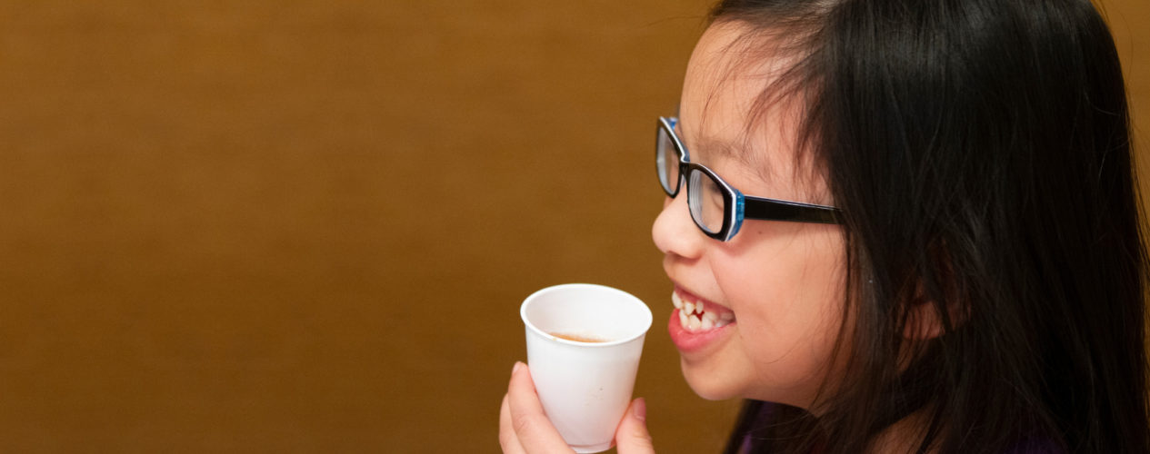 An elementary aged girl drinks out of a paper cup.
