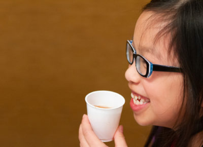 An elementary aged girl drinks out of a paper cup.