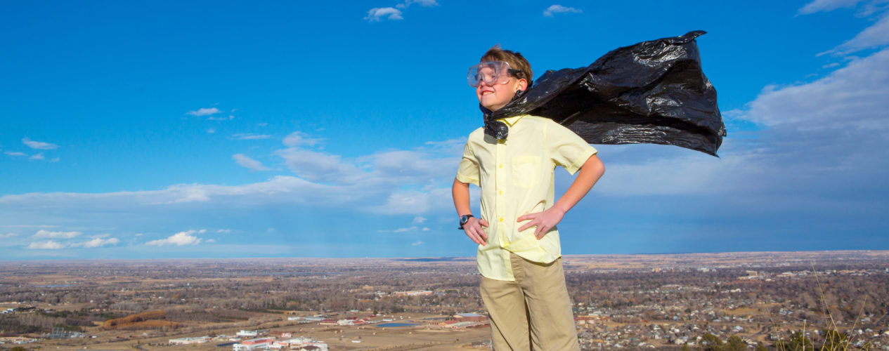 A child standing on a hill with a black superhero cape blowing int he wind.