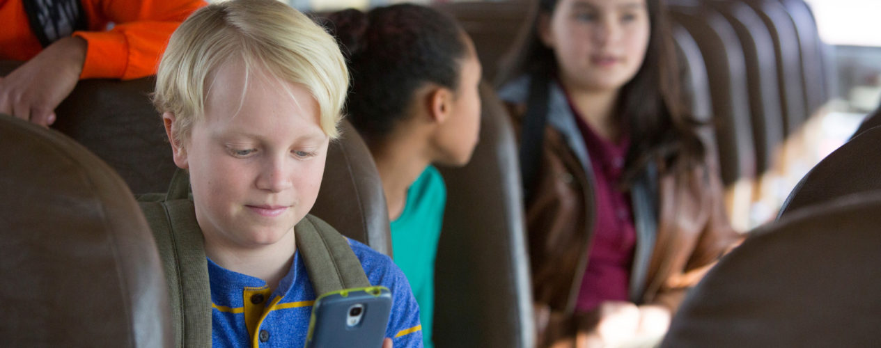 A preteen boy sits on his school bus looking at his phone to avoid peer pressure.