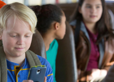 A preteen boy sits on his school bus looking at his phone to avoid peer pressure.