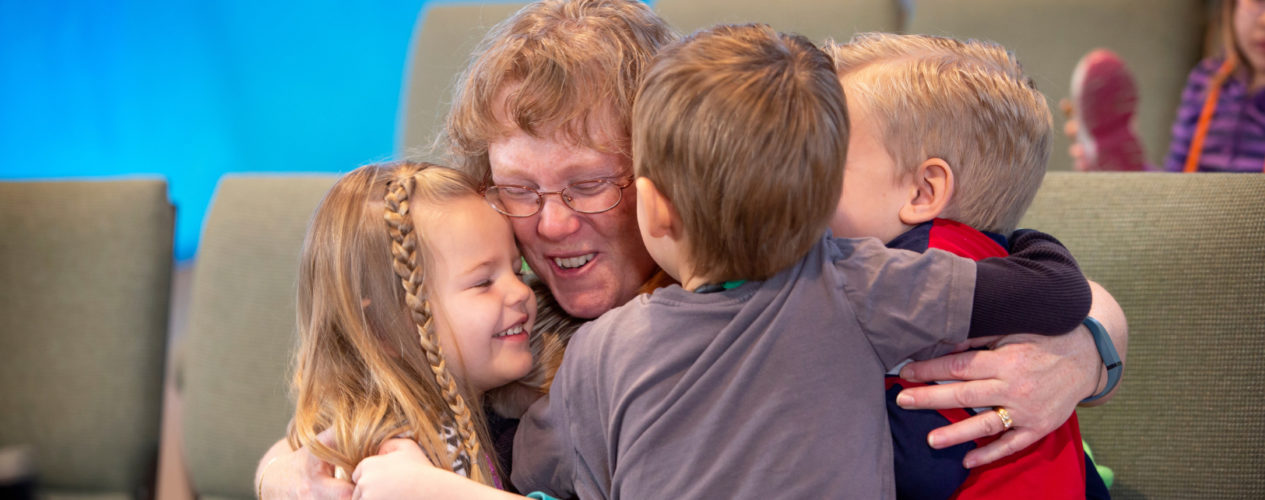 An older female volunteer receives a group hug from her group of preschoolers.