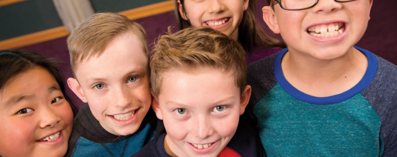 A group of five old elementary aged kids gathered around and smiling after playing an indoor game.