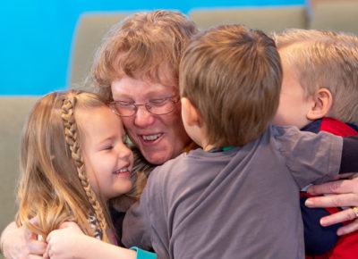An older woman volunteer is hugging her small group of children.