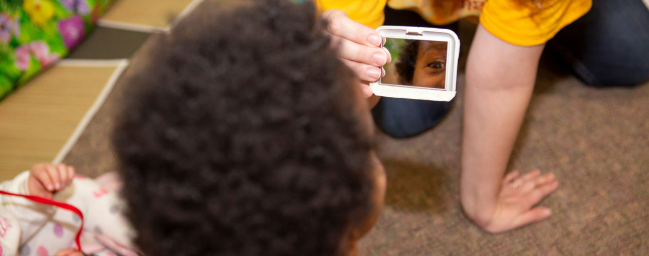 A preschool boy is looking in a mirror for a Martin Luther King Jr. Day lesson..