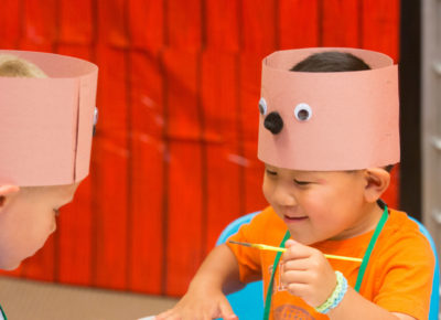 Three preschoolers wearing bear hats smiling as the paint.