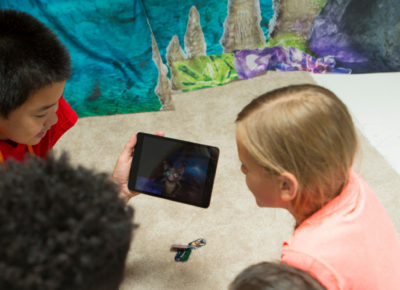 A group of older elementary students gathering around a small tablet.