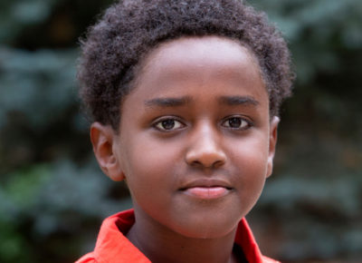 A preteen boy stares straight at the camera as he stands outside.