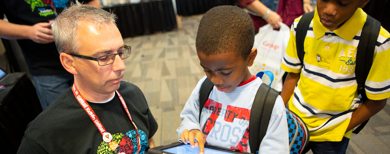 A children's ministry director showing two boys a trending game on an iPad.