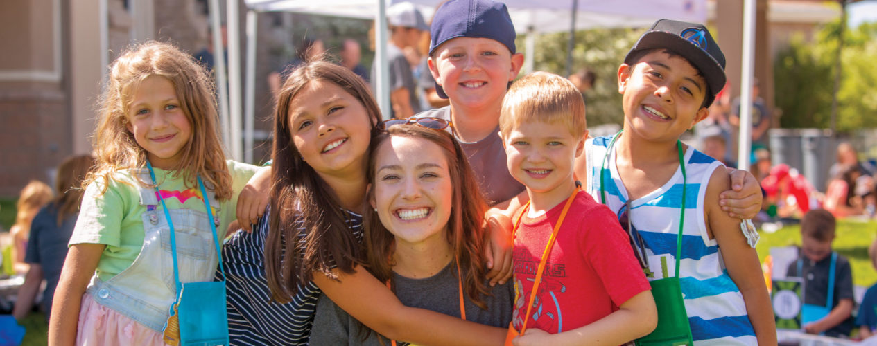 A VBS crew leader is smiling as she is hugged by five of her kids.
