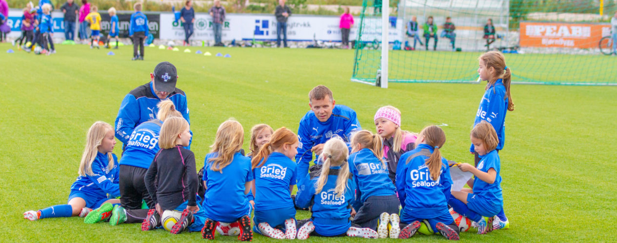 A girls elementary soccer team is huddled around on the soccer field.