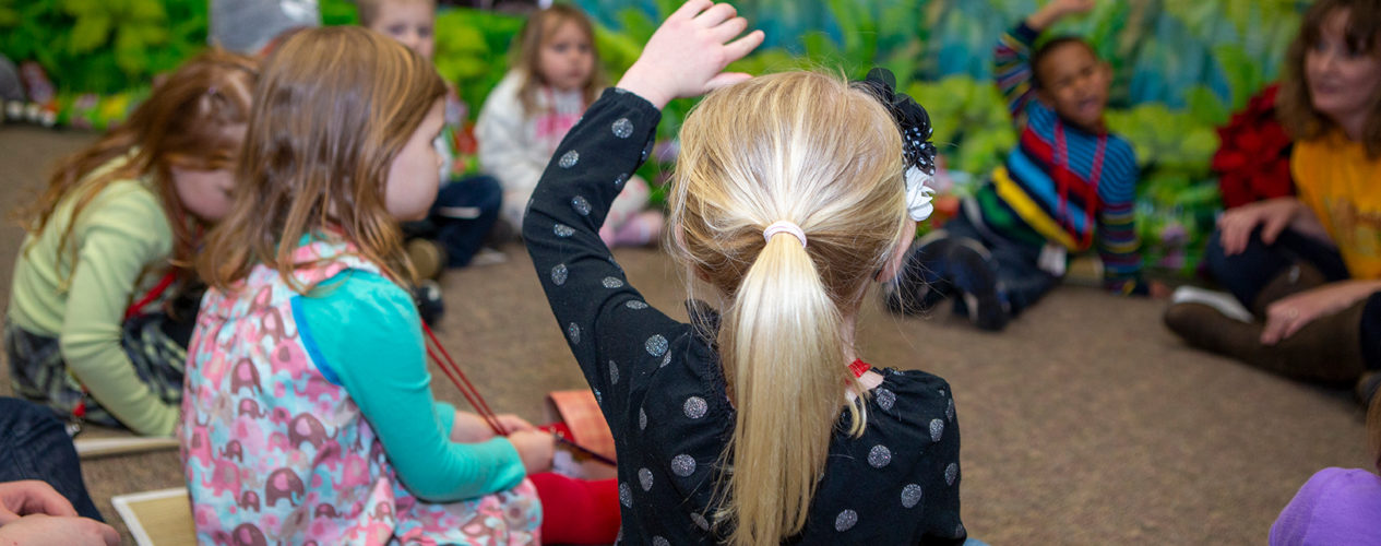 A preschool girl raises her hand to answer a question.