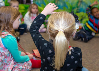 A preschool girl raises her hand to answer a question.
