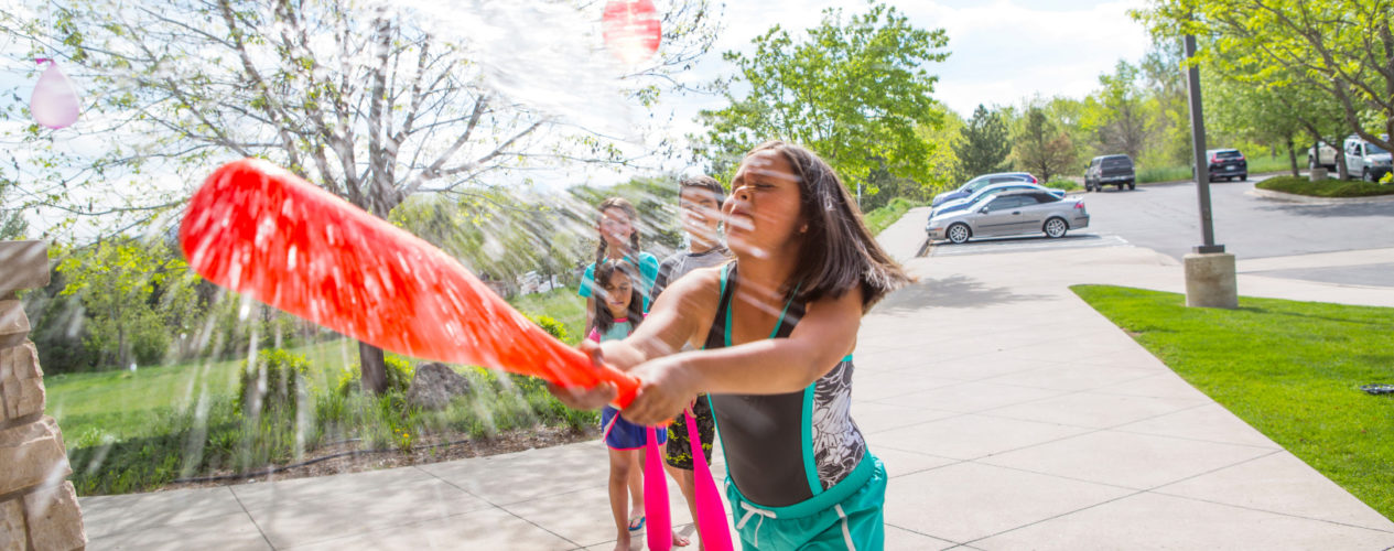 A girl hitting a water balloon with a plastic bat. This is a summer outreach activity that can be used all year long.