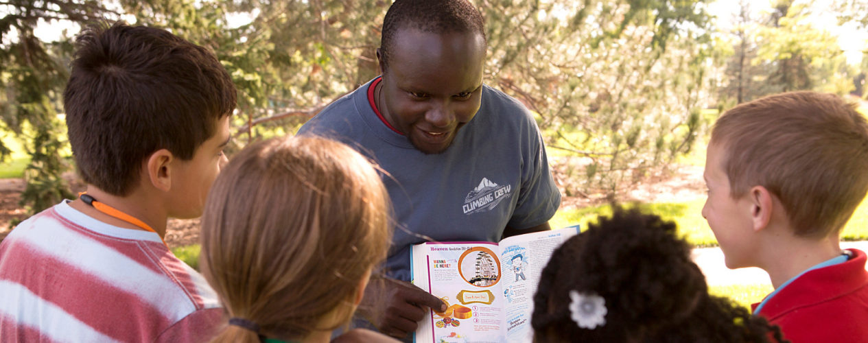 An adult leader shows his four students a passage in the Bible.