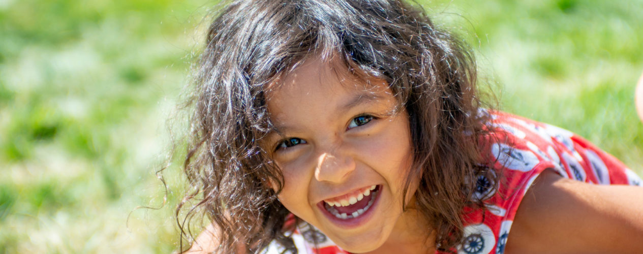 A preschool girl with diabetes smiles as she plays outside.