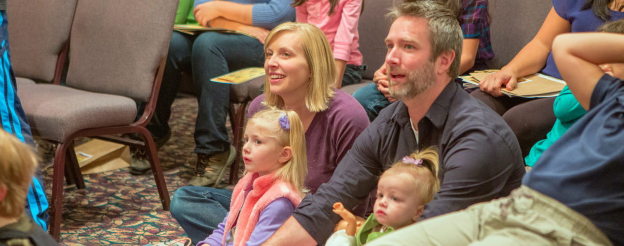 A mom and dad sitting on the ground with their two young daughters at a family ministry event.
