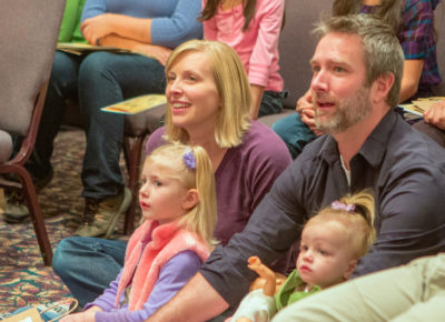 A mom and dad sitting on the ground with their two young daughters at a family ministry event.