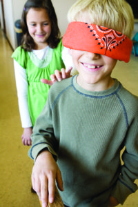 A girl taps the shoulder of a boy who's wearing a blindfold.