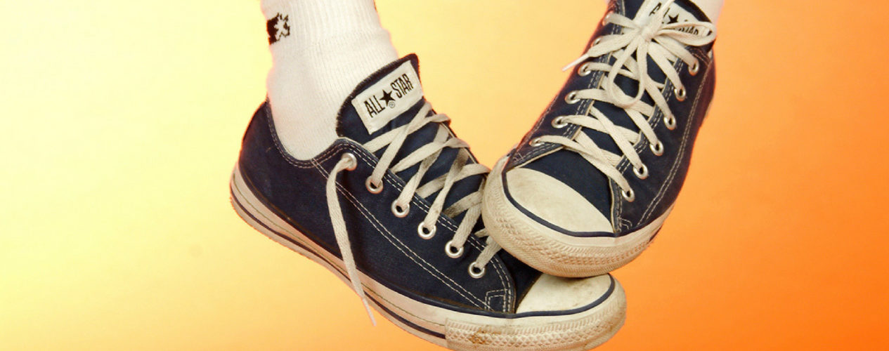 A pair of black converse All-Stars on a pair of feet. The background is a bright orange and yellow.