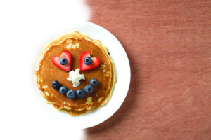 A stack of pancakes with a smilie face made of berries.