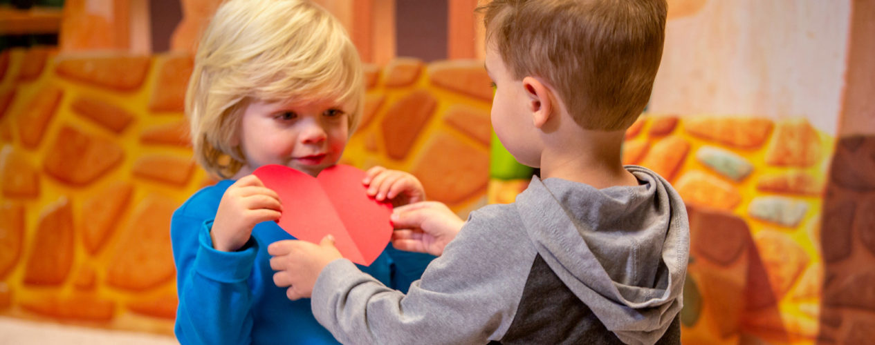During one of the valentine's day ideas, two preschool boys are passing a construction paper heart back and forth.