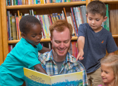 A male volunteer reads to three preschool kids.