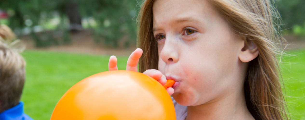 A preteen girl inflating an orange balloon.