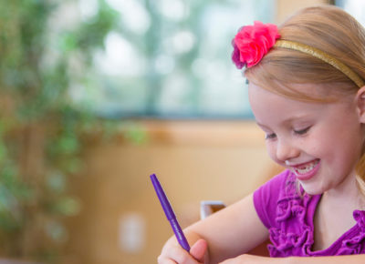 An elementary aged girl writing on a piece of paper as she smiles.