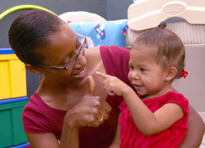A nursery volunteer does a finger play with a baby.