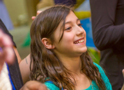 A preteen girl smiles as she lifts her arms in excitment.