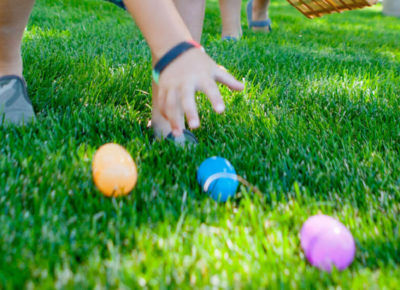 A child's hand goes to grab a blue Easter egg that's laying on the ground.