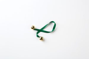 Two small bells attached to a dark green piece of ribbon.