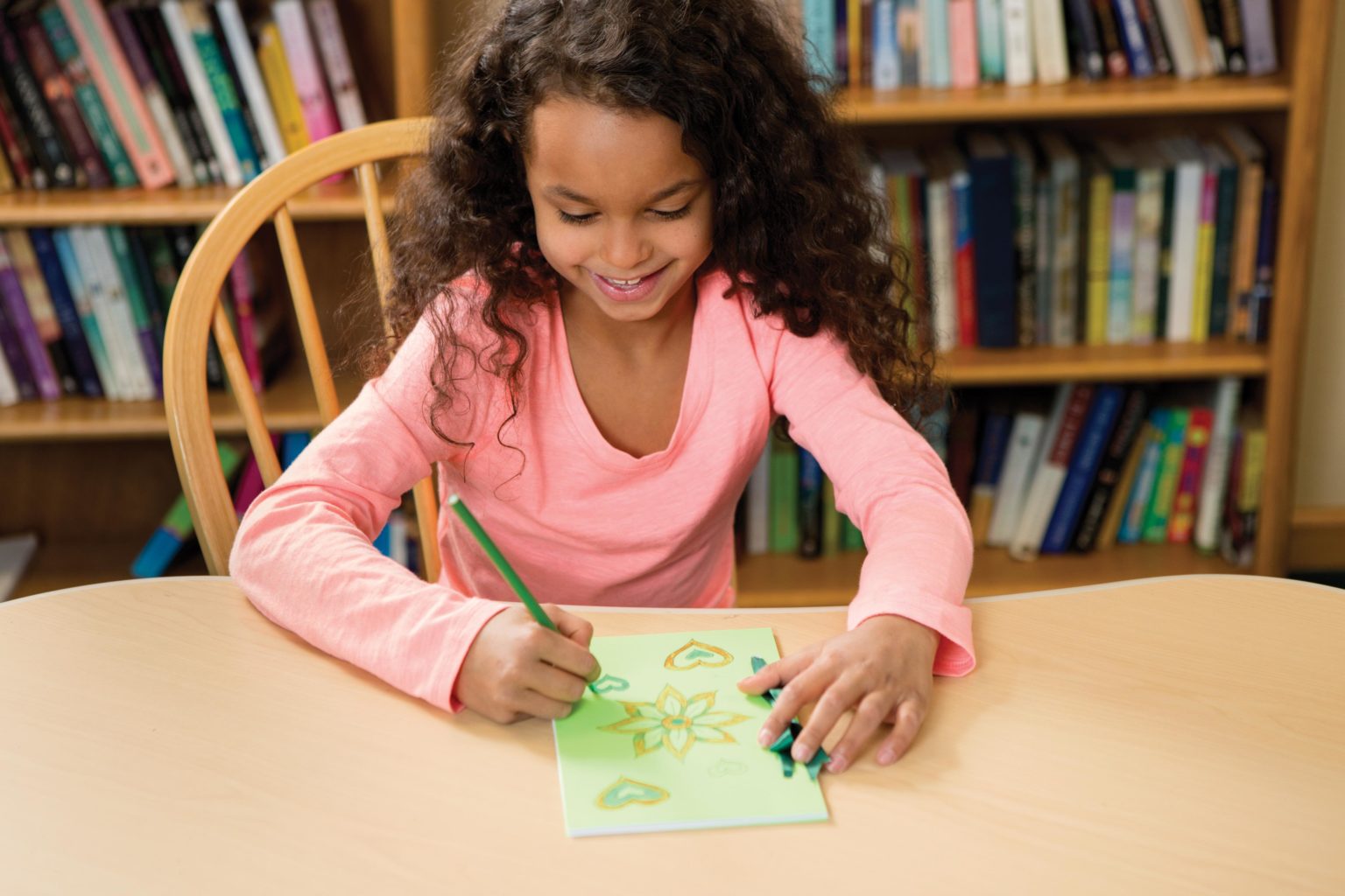 An elementary girl creates a card at a table.