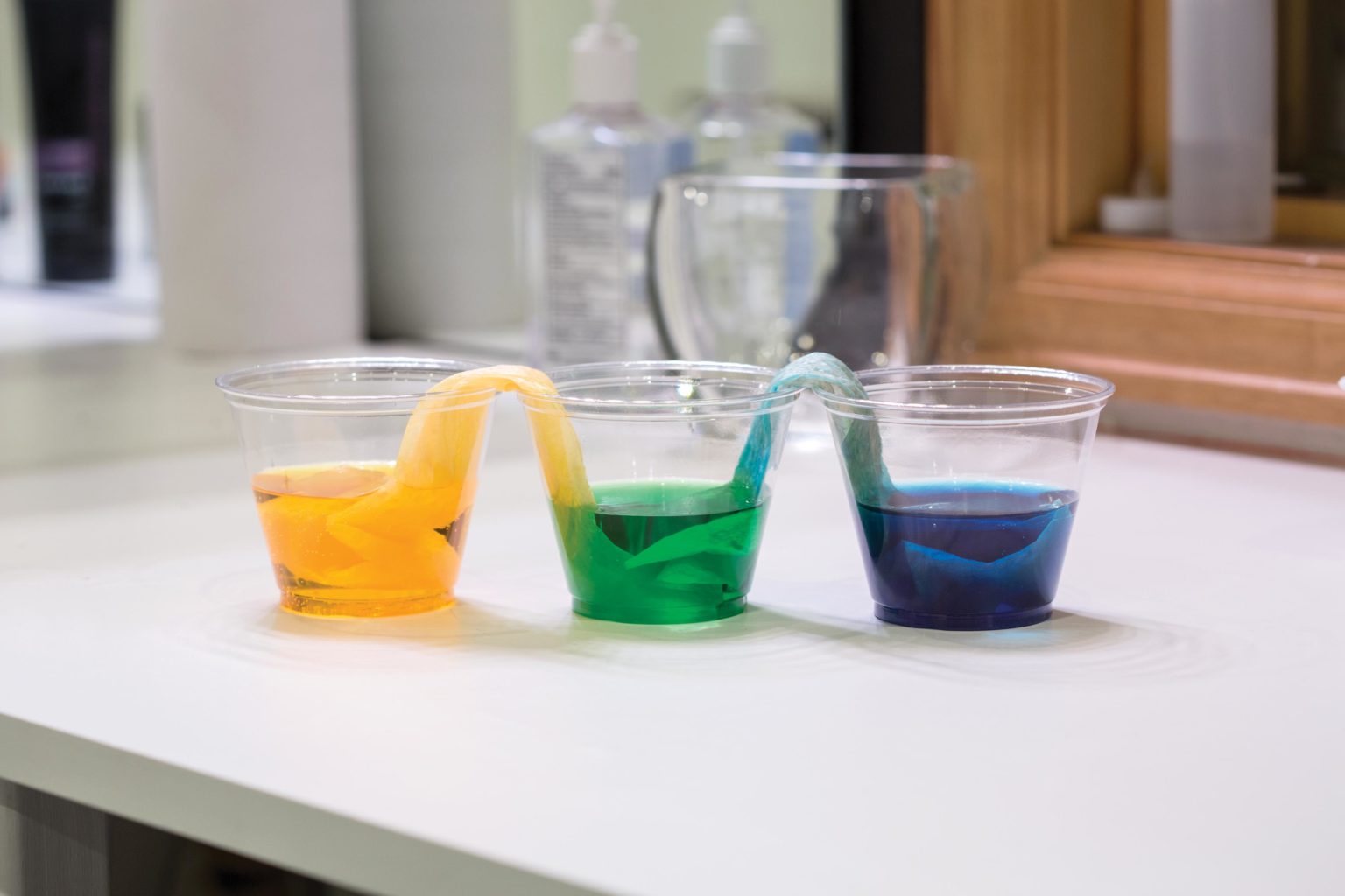 Three plastic cups with paper towels linking them. One cup is yellow and one is blue. The cup that joins the two is green.
